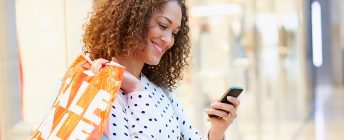 Woman holding shopping bags and looking down at smartphone