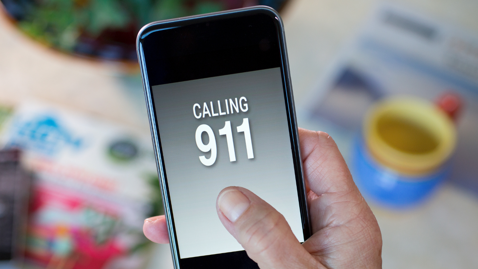 Man's hand holding up smartphone with the number 911 on the screen